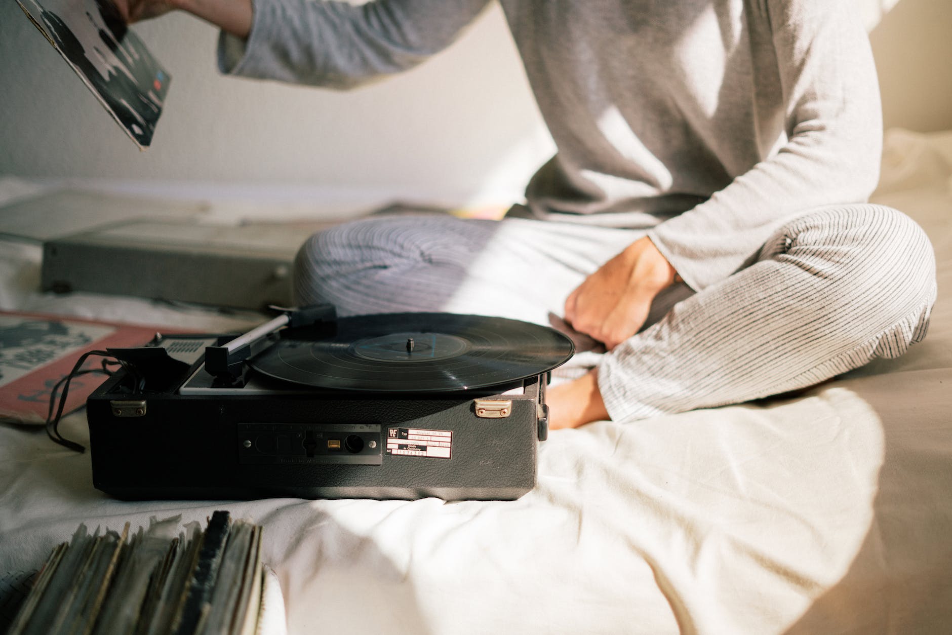 person in gray sweater holding black vinyl record player